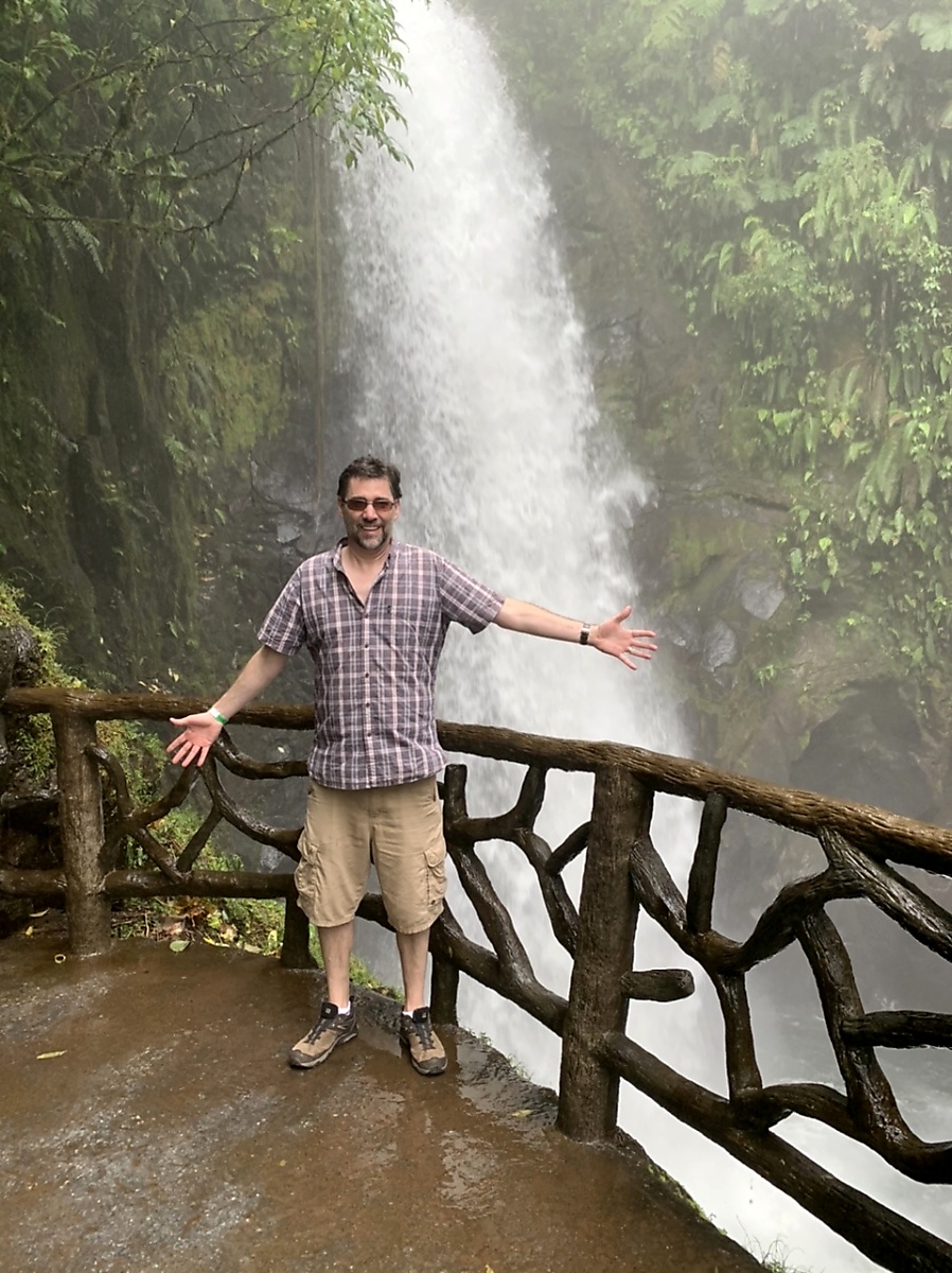 The Thorough Tripper standing in front of rushing waterfall at La Paz Waterfall Park in Costa Rica
