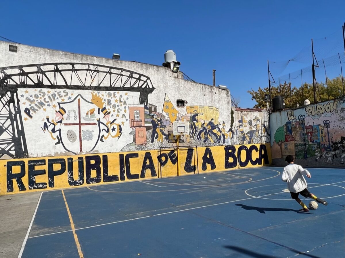 A boy kicks a football against The Republica de La Boca mural