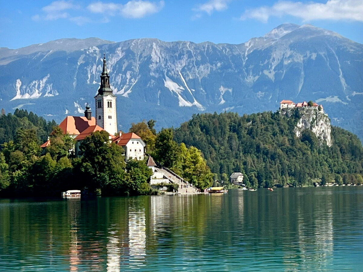 A scenic view of Lake Bled, Lake Bled Island, it's church and Bled Castle with the Julian Alps in the background