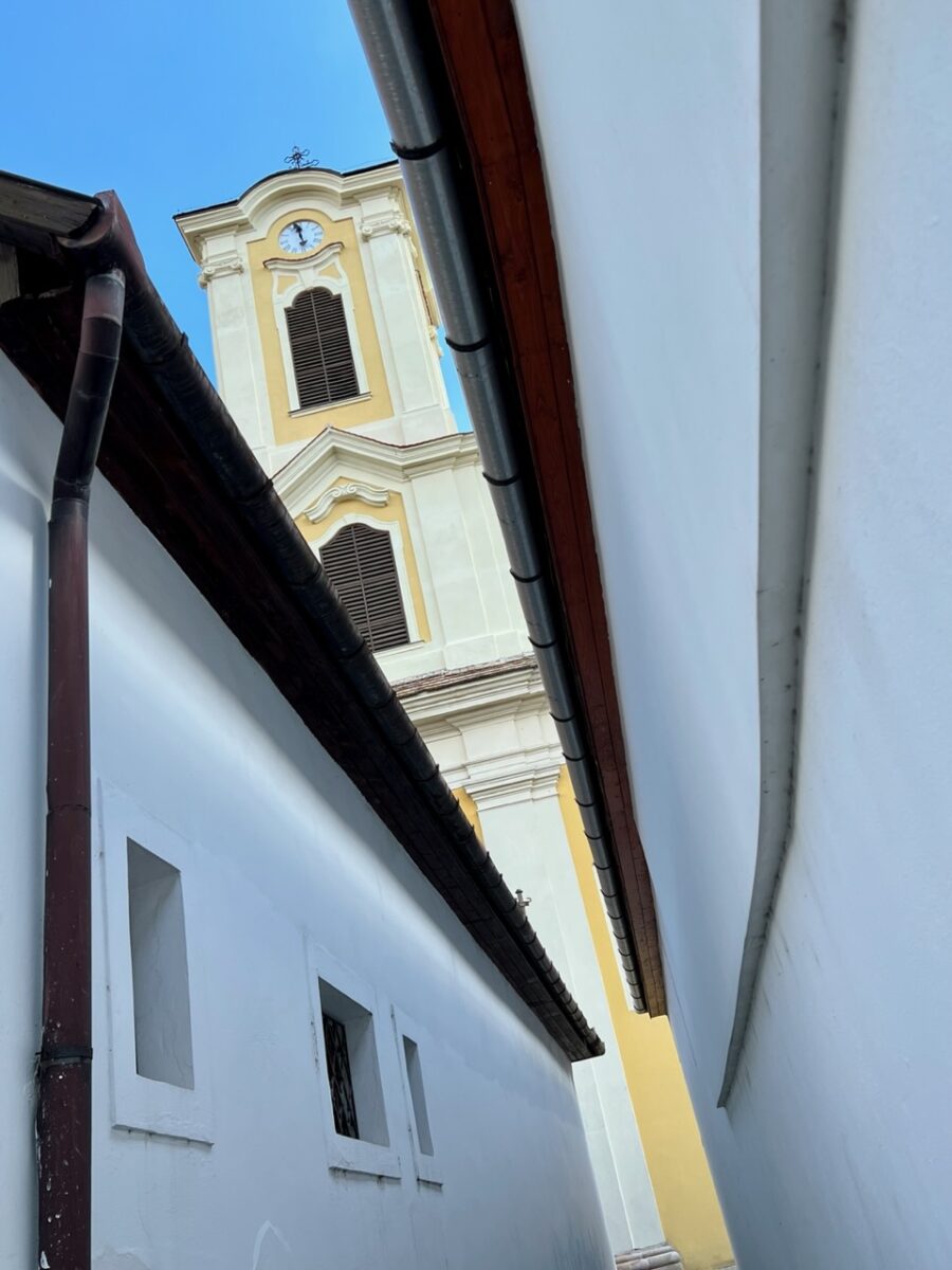 Peaking through white buildings to a yellow church tower in Szentendre Hungary while on an easy day trip from Budapest
