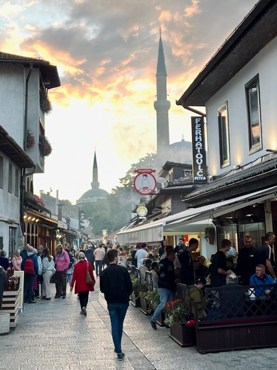 A street in the Baščaršija area of Sarajevo at sunset with the outlines of two mosques