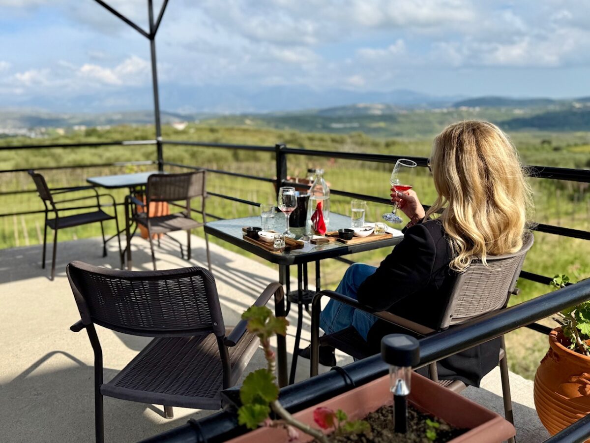 A woman enjoys a glass of wine and a vineyard view as part of a wine tasting at Stilianou Winery in Crete