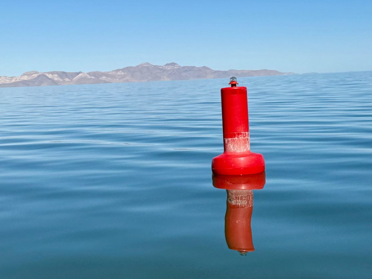 A red buoy floating on the Great Salt Lake with Antelope Island in the distance