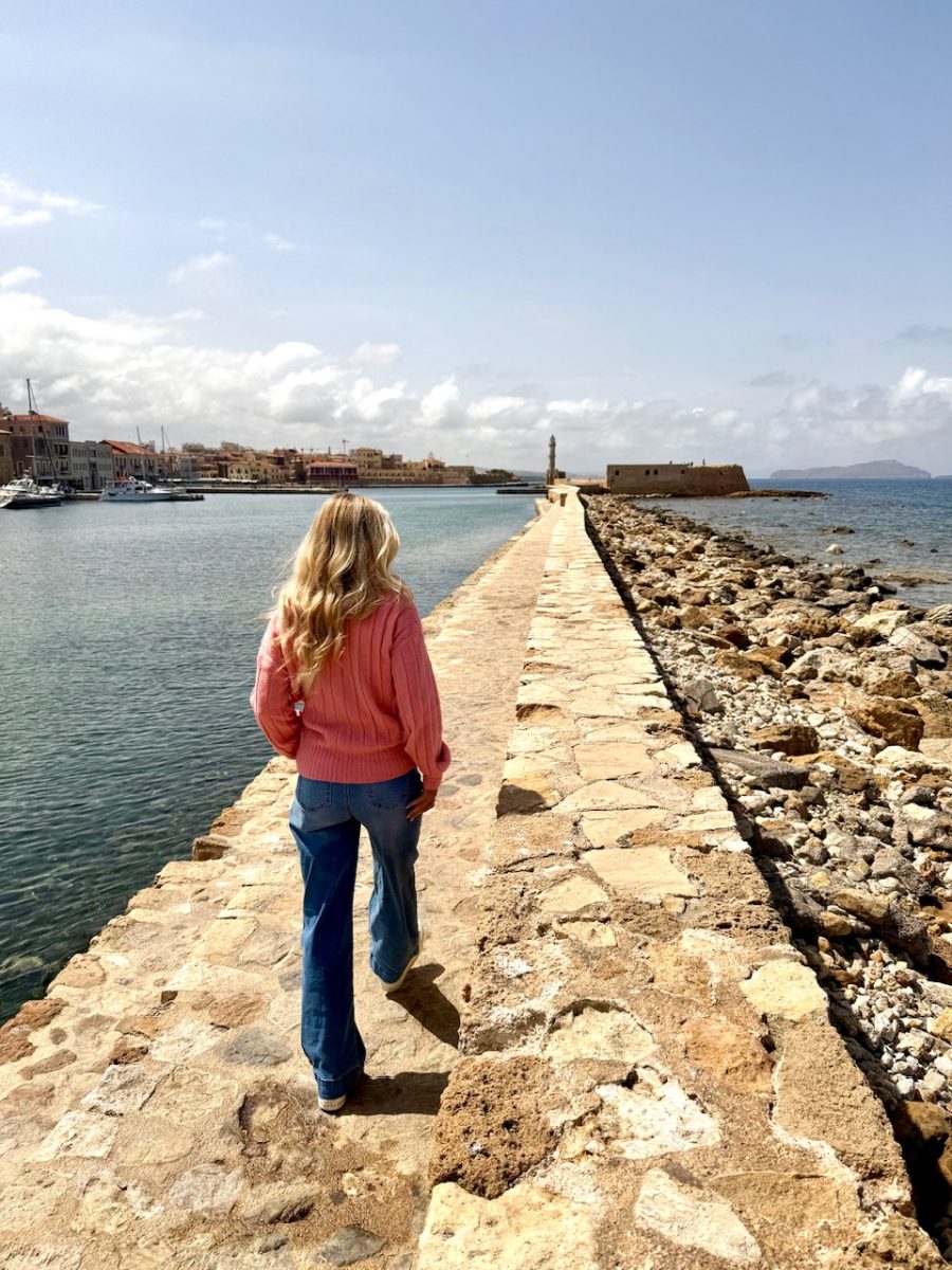 A woman walks along the sea wall of the Venetian Harbor which is one of the very best things to do in Chania Crete